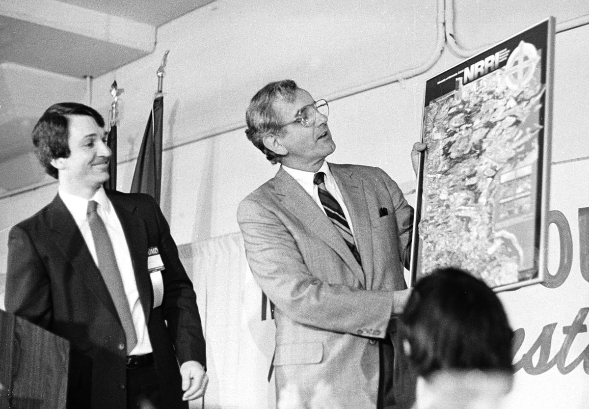 Black and white image of two men, one holding an illustrated map of Minnesota.