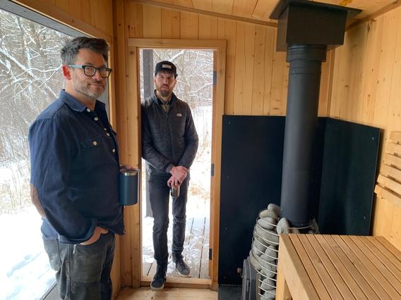 Two men stand inside a sauna.