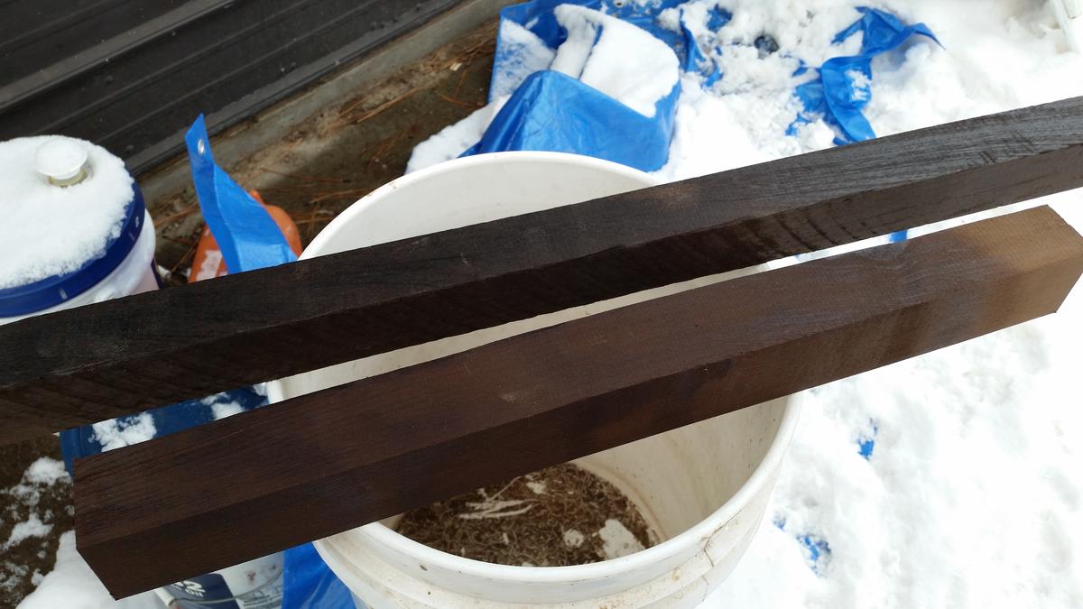 Two lengths of wood, one dark brown, one almost black, are posed on a white bucket.
