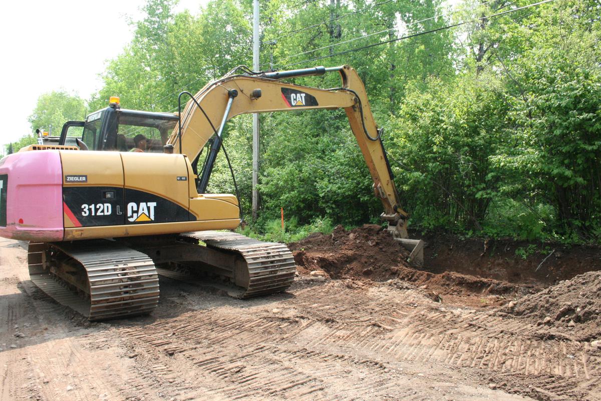An excavator in operation on a dirt road digging a ditch