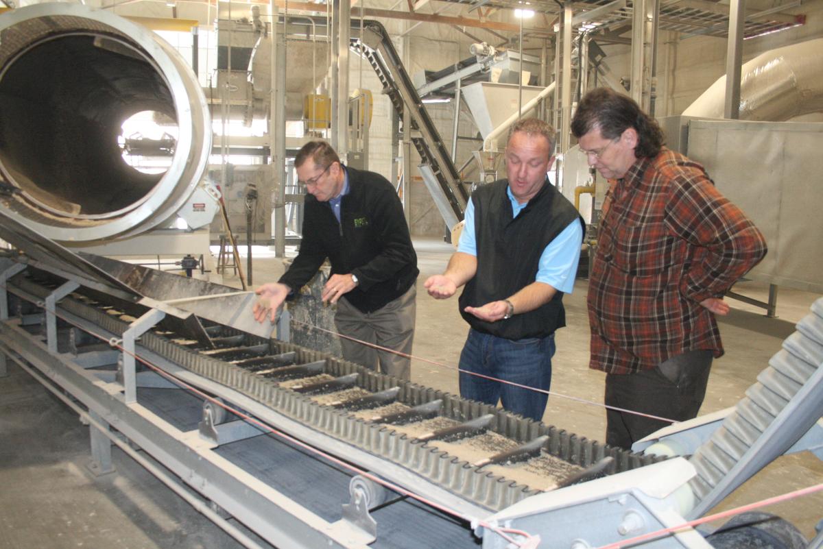 Three men looking at white product on conveyor belt production line.