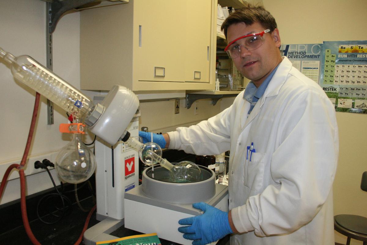 Man in white lab coat using chemistry apparatus in a lab.