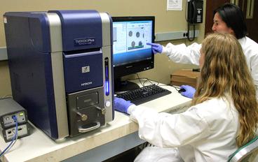 Scanning Electron Microscope with two lab technicians looking at monitor.</body></html>