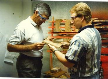 Two men in safety glasses inspect a piece of wood