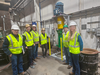 Six people in safety vests and hard hats stand near an upright piece of equipment